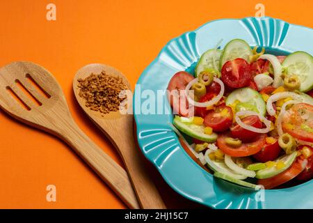 Goiania, Goias, Brésil – 25 janvier 2021 : une assiette avec salade de légumes et deux couverts en bois sur fond orange. Banque D'Images