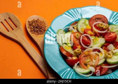 Goiania, Goias, Brésil – 25 janvier 2021 : une assiette avec salade de légumes et deux couverts en bois sur fond orange. Banque D'Images