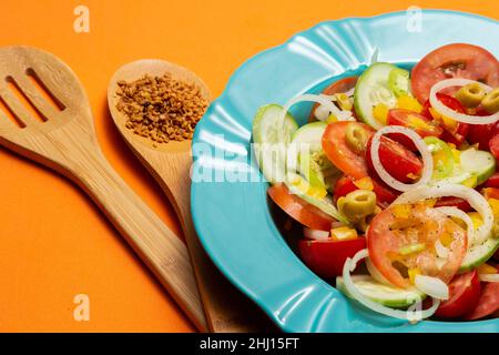 Goiania, Goias, Brésil – 25 janvier 2021 : une assiette avec salade de légumes et deux couverts en bois sur fond orange. Banque D'Images