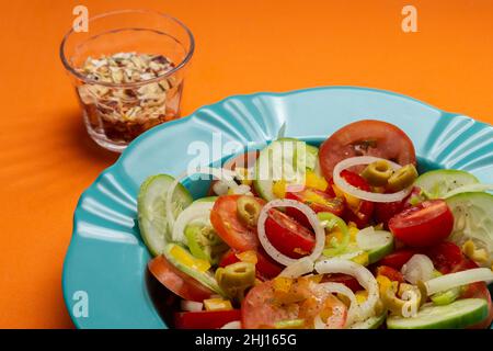 Goiania, Goias, Brésil – le 25 janvier 2021 : une assiette de salade de légumes à fond orange et un verre de assaisonnements déshydratés. Banque D'Images