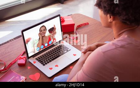 Bonne jeune femme caucasienne avec du vin pendant la rencontre en ligne avec le petit ami biracial le jour de la Saint-Valentin. Non modifié, rencontres en ligne, appel vidéo et distant Banque D'Images