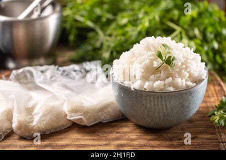 Riz cuit dans un bol avec riz cru dans des sachets de plastick. Banque D'Images