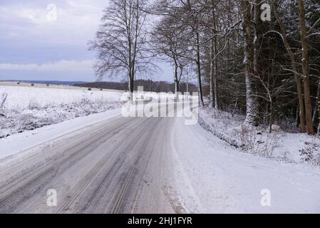 Route asphaltée étroite dans la forêt.Les chaussées et la route sont recouvertes d'une couche de neige.Vous pouvez voir les pistes des roues des voitures. Banque D'Images