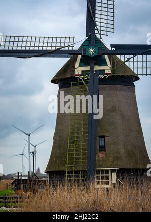 Moulin historique hollandais devant les éoliennes modernes, comparaison des technologies anciennes et nouvelles Banque D'Images