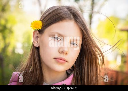 Belle petite fille blonde avec fleur de pissenlit jaune dans les cheveux, portrait d'été extérieur Banque D'Images