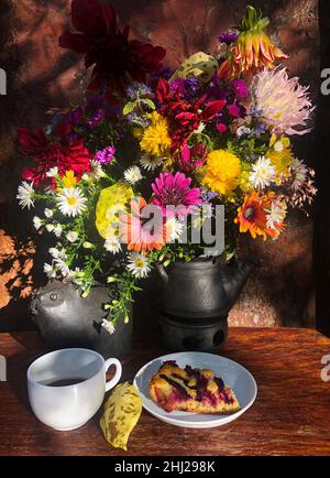 Un bouquet de fleurs d'automne dans un vase en céramique, une tasse de café, une figurine d'argile d'un chat et une tarte aux baies aux rayons du soleil d'automne. Banque D'Images