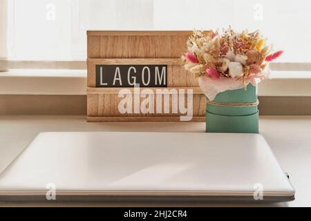 Beau bouquet de fleurs séchées et panneau en bois avec texte LAGOM sur table blanche à côté de l'ordinateur portable Banque D'Images