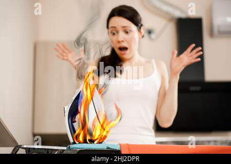 Une femme crie dans la panique quand elle voit un fer brûlant. Causes d'inflammation et d'incendie dans le boîtier. Sécurité incendie et extinction d'incendie. Banque D'Images