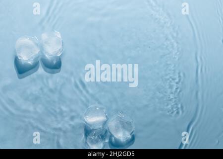 Glaçons avec gouttes d'eau dispersées sur fond bleu, vue du dessus. Banque D'Images