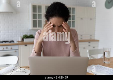 Une jeune femme fatiguée se sent mal en s'asseyant près d'un ordinateur portable Banque D'Images