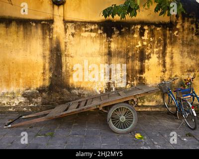 Une vieille charrette et des vélos modernes sur le fond de l'ancien mur jaune dans la ville antique de Hoi an, Vietnam Banque D'Images