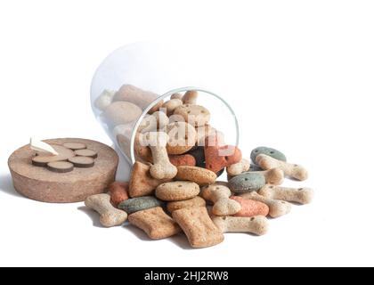 Gâteries ou biscuit pour chiens de différentes couleurs et formes dans un pot en verre avec couvercle sur fond blanc Banque D'Images