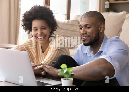 Un couple africain joyeux s'assoit dans un salon confortable avec un ordinateur portable Banque D'Images