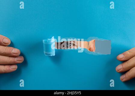 l'œil d'un homme regardant à travers la déchirure dans une feuille de papier Banque D'Images