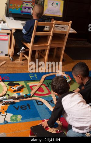 Éducation préscolaire 4-5 ans deux garçons jouant avec set, garçon en arrière-plan utilisant le bureau en arrière-plan Banque D'Images