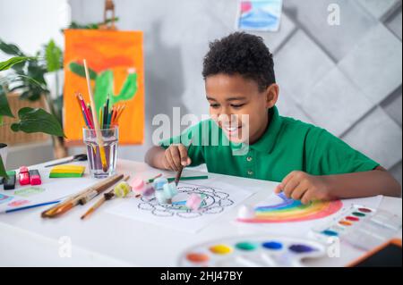 Garçon assis à la table poussant des tubes de peinture Banque D'Images