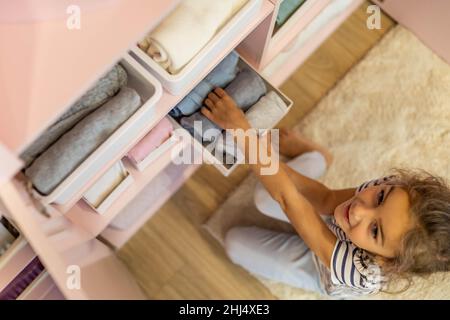 Vue du dessus petite fille a soigneusement plié les vêtements dans la boîte de rangement pour un rangement vertical confortable sur les étagères Banque D'Images