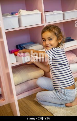 Vue du dessus petite fille a soigneusement plié les vêtements dans la boîte de rangement pour un rangement vertical confortable sur les étagères Banque D'Images