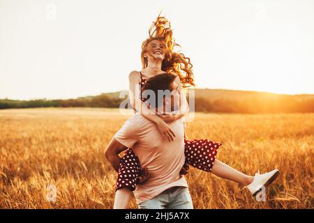 Homme et femme passant la Saint-Valentin à marcher dans le champ de blé, souriant et s'amusant ensemble.Homme donnant à sa petite amie terrain de blé de porc-back Banque D'Images
