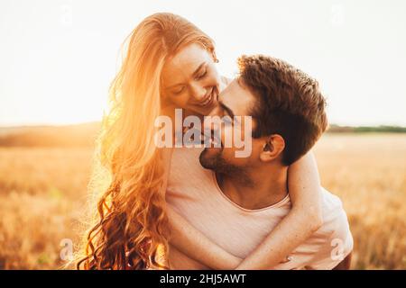 Portrait en gros plan d'une fille aux cheveux rouges avec un visage défoncé debout derrière son mari et embrassant son cou au soleil.Pour un style de vie Banque D'Images