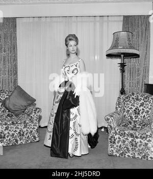 Mylène Demongeot, actrice française, donne un aperçu de la robe qu'elle portera au premier ministre de son nouveau film, la chanteuse Not the Song, à l'Odeon, Leicester Square demain soir, photographiée dans sa chambre à l'hôtel Dorchester, Londres, le mercredi 4th janvier 1961.Mylène Demongeot porte une robe longue à jupe pleine longueur de satin blanc et brodée avec des paillettes noires et blanches dans un motif de feuilles, avec une grande ceinture de satin noir qui se lie dans un noeud à la taille, complétée par une stole de renard blanc. Banque D'Images