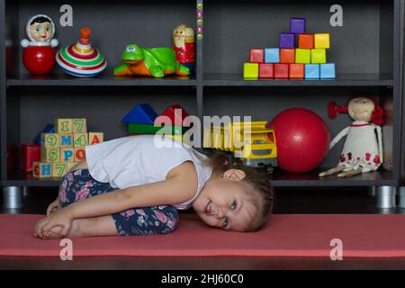 La petite fille se trouve dans le yoga de l'enfant poser comme s'asseoir sur les talons, amener le front vers le bas pour reposer devant les genoux, poser vos bras le long du corps Banque D'Images