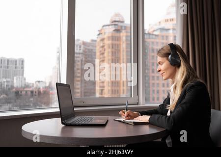 femme d'affaires caucasienne travaillant dans un bureau lumineux avec un ordinateur portable, un webinaire ou une conférence en ligne à l'écoute dans un casque, travaillant sur de nouvelles affaires de projet Banque D'Images