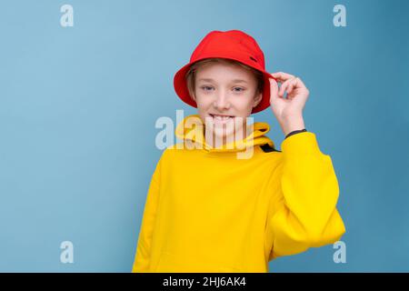 Portrait d'un homme positif dans une veste jaune et un chapeau de panama rouge sur fond bleu, regardant l'appareil photo avec un sourire sur son visage.Un adolescent caucasien heureux posant dans un joli studio souriant Banque D'Images