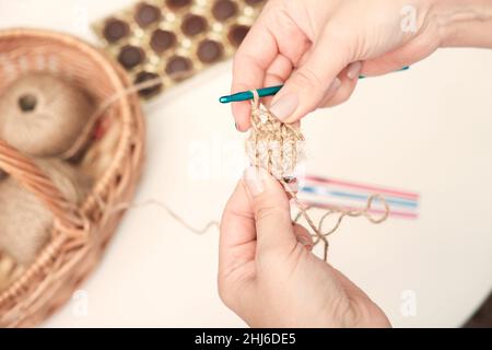 mains d'une femme tenant des fils de crochet et de jute et fragment d'un motif tricoté. tricot écologique naturel, dessous-de-verre fait main. artisanat et passe-temps, décoration écologique Banque D'Images