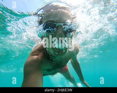 Vue sous-marine d'un plongeur jeune homme nager dans la mer. Des bulles d'air sortant de la bouche et le nez Banque D'Images