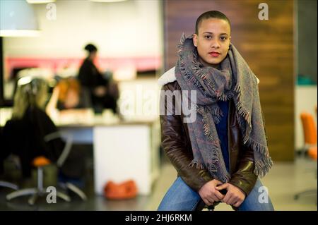 Tilburg, pays-Bas. Portrait d'un coiffeur et d'un coiffeur féminin d'origine africaine, portant une veste et un châle et assis sur un tabouret à l'intérieur d'un salon de coiffure de centre-ville. Banque D'Images