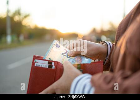 Une femelle méconnaissable prend un billet de 20 euros dans un portefeuille en cuir rouge dans la rue.Paiement, salaire et concept bancaire. Banque D'Images