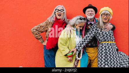 Des personnes âgées dynamiques qui ont passé un bon moment tout en se tenant ensemble sur un fond rouge.Groupe d'amis âgés joyeux célébrant leur retraité Banque D'Images