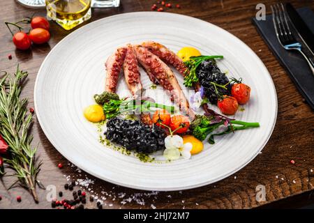 Poulpe avec risotto noir. Crème de carottes, mini-brocoli, pesto de basilic. Une délicieuse cuisine traditionnelle saine est servie pour le déjeuner dans une cuisine gastronomique moderne Banque D'Images