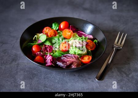 Une salade de laitue, de tomate, de laitue d'agneau et d'escamole sur une assiette noire sur fond d'ardoise Banque D'Images