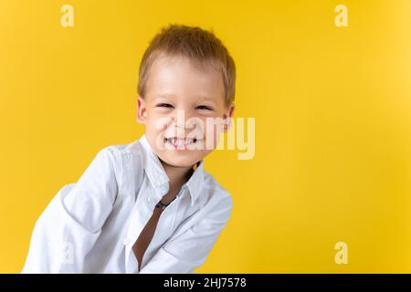 Bannière Funny Preschool Child Boy en chemise sans bouton sourire œil étroit sur fond jaune espace de copie. Joyeux sourire à l'école Banque D'Images