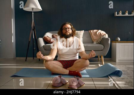 Drôle d'homme gras méditant pratiquant le yoga à la maison Banque D'Images