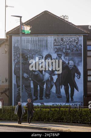 Les gens marchent devant la fresque commémorative du dimanche sanglant à Derry, en Irlande du Nord, qui dépeint la mort de Jackie Duddy avec le P. Edward Daly. Banque D'Images