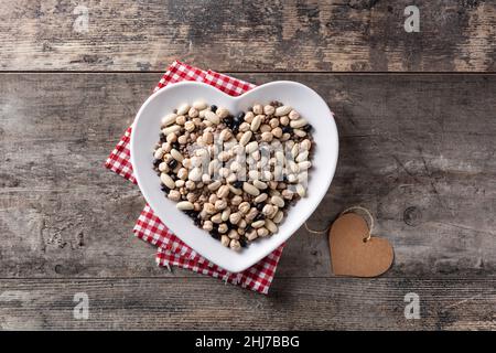 Légumes assortis non cuits dans une assiette en forme de coeur sur une table en bois Banque D'Images