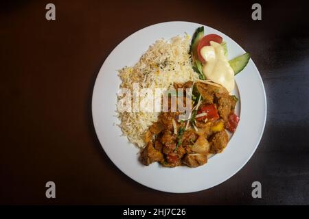 Viande et légumes cuits dans une sauce épicée, curry indien avec riz et décoration de salade sur une assiette blanche et une table en bois marron, espace copie, haut A. Banque D'Images