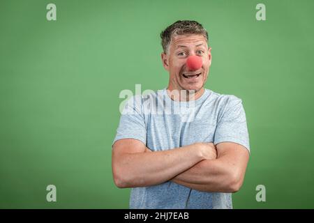 homme au nez clown rouge et chemise grise sur fond vert Banque D'Images