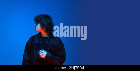 Portrait d'un jeune homme triste, étudiant posant isolé sur fond bleu à la lumière du néon.Concept d'émotions, d'étude, d'éducation, de mode Banque D'Images