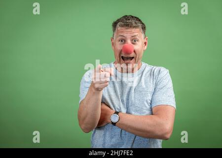 homme au nez clown rouge et chemise grise sur fond vert Banque D'Images