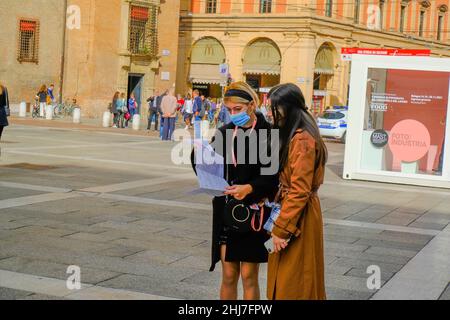 Octobre 2021 Bologne, Italie: Deux jeunes femmes en vêtements élégants portant des masques médicaux et étudiant la carte de la ville près de la fontaine Neptune sur le Banque D'Images