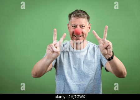 homme au nez clown rouge et chemise grise sur fond vert Banque D'Images