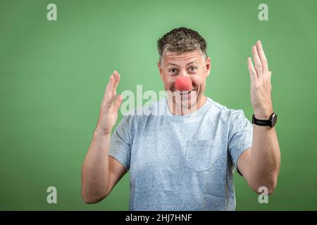 homme au nez clown rouge et chemise grise sur fond vert Banque D'Images