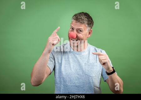 homme au nez clown rouge et chemise grise sur fond vert Banque D'Images