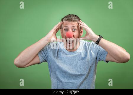 homme au nez clown rouge et chemise grise sur fond vert Banque D'Images