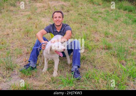 Homme avec un chien blanc d'une race de laggoto-Romagnolo assis sur l'herbe dans le parc.Marche du chien dans le parc. Chien à la recherche de champignons de truffe Banque D'Images