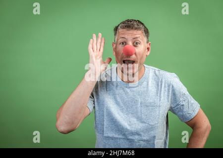 homme au nez clown rouge et chemise grise sur fond vert Banque D'Images